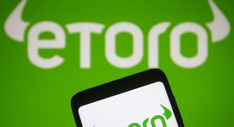 An eToro logo is seen on a smartphone and a computer screen.
