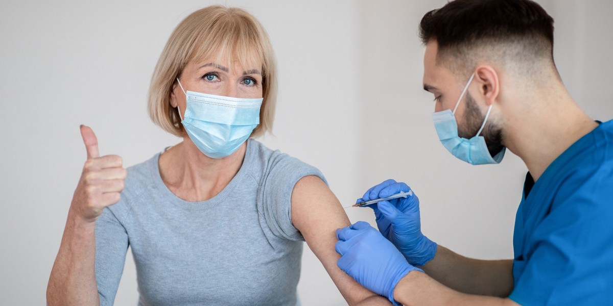 Mature woman in face mask approving of covid-19 vaccination, showing thumb up during coronavirus vac