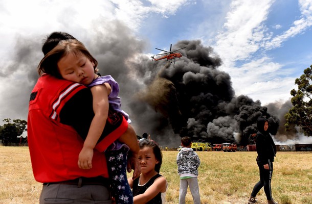 Local residents watch as a helicopter, known as 'Elvis', drops water onto a pile of burning tyres in