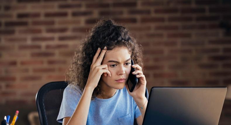 Curly haired woman working at laptop troubleshooting on the phone