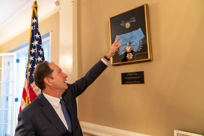 El embajador de Estados Unidos en Polonia, Mark Brezhinsky, muestra dos de las principales condecoraciones de su padre: la Medalla Presidencial de Estados Unidos y la Orden del Águila Blanca de Polonia.  Ambas medallas están colgadas hoy en su casa de Varsovia