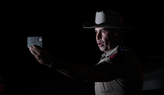 Funkcjonariusz policji stanowej Teksasu rozmawia przez telefon, podczas gdy śledczy pracują na miejscu strzelaniny