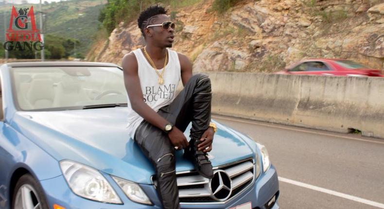 Shatta Wale sitting on a car