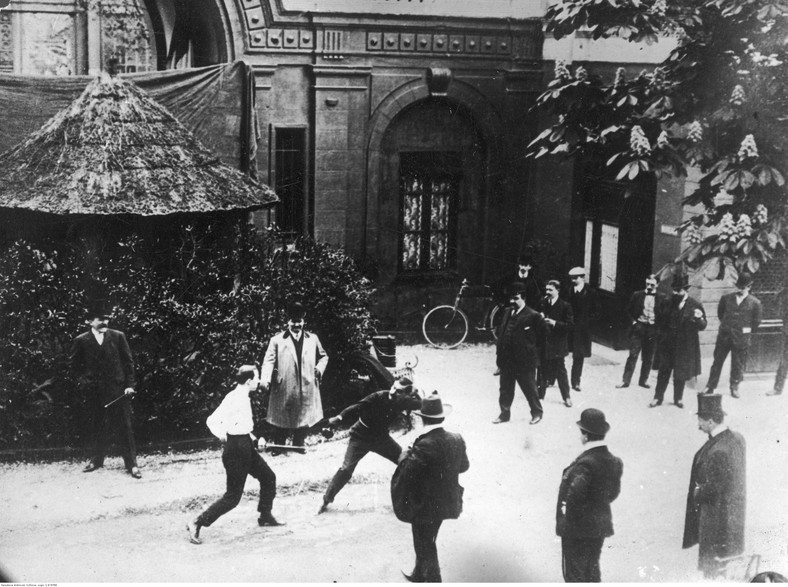 Uliczny pojedynek na broń białą. Mężczyźni pojedynkują się przy użyciu floretów w otoczeniu gapiów (1930 r.)