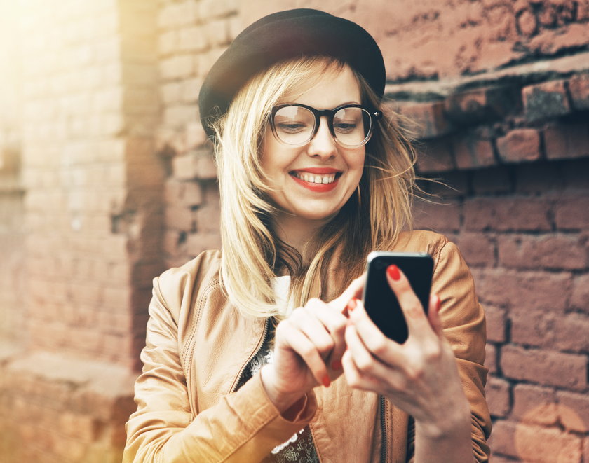 City lifestyle stylish hipster girl using a phone texting on smartphone app in a street