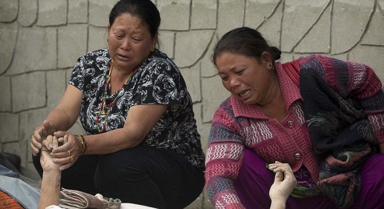 Grieving women hold the hands of relatives as they lie beneath a thin white sheet in the city of Kathmandu.