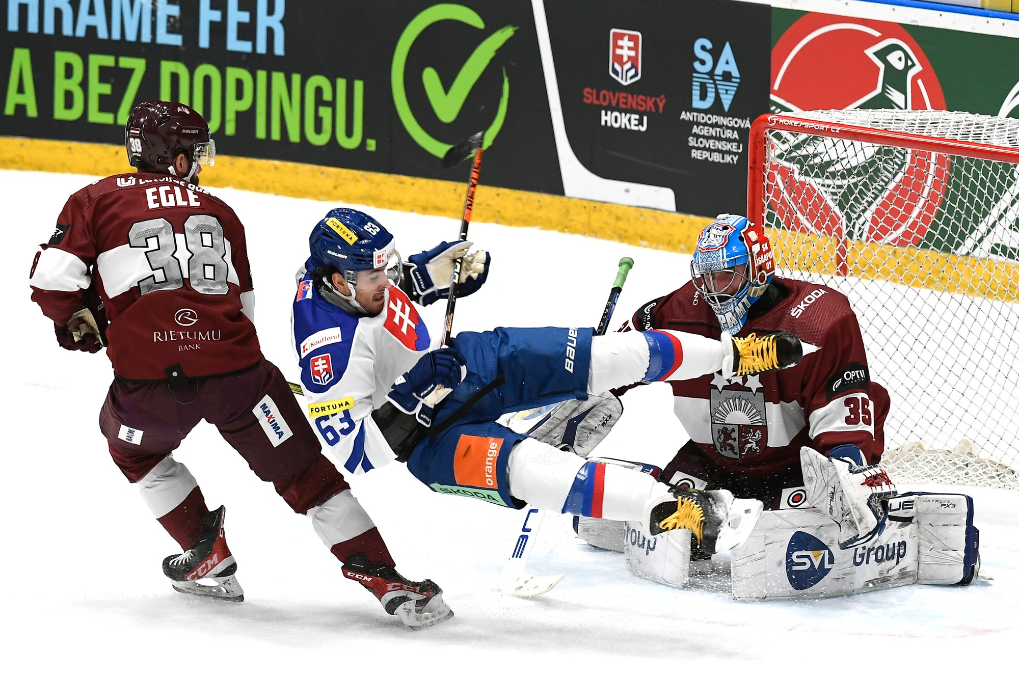 Patrik Lamper (Slovensko), vľavo Haralds Egle a vpravo brankár Eriks Vitols (obaja Lotyšsko) bojujú o puk.