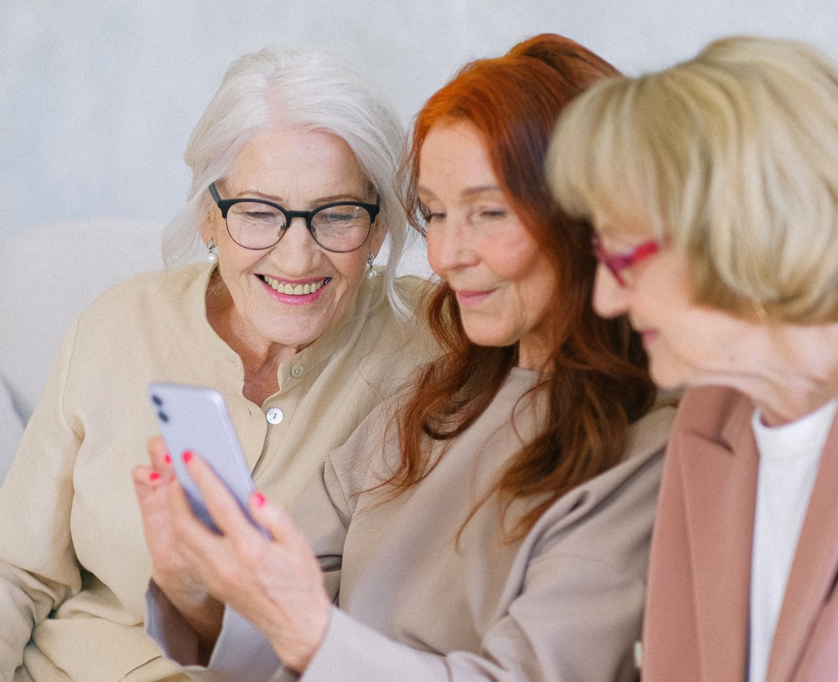 Trzy seniorki patrzą w ekran jednego smartfona