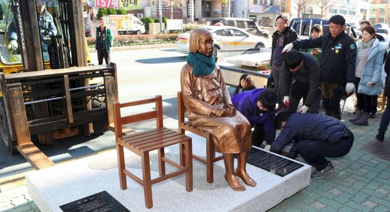 Workers setting up a statue of a teenage girl symbolizing comfort women who served as sex slaves for Japanese soldiers during World War II outside the Japanese consulate in Busan