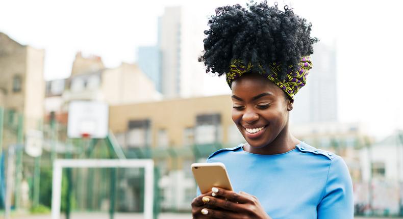 A woman smiling while looking at her phone [Photo: Courtesy]