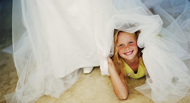 A young girl hides underneath a bride's dress at a weddingLaurence Monneret/Getty Images