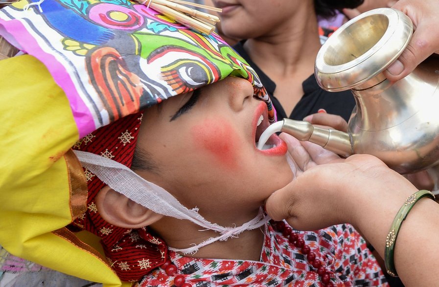 Nepalka wlewa mleko do ust chłopca podczas procesji na festiwal krów Gai Jatra w Katmandu, 16 sierpnia 2019 r.