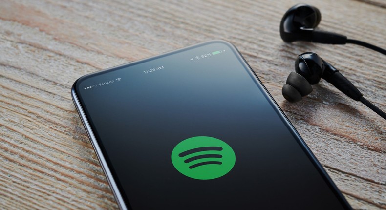 An Android smartphone with the Spotify Music logo visible on screen, alongside a pair of earphones.
