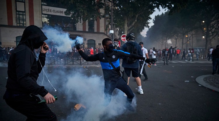 PARIS, FRANCE - AUGUST 23: A Paris Saint Germain fan throws a tear gas shell towards French Riot Police during violent confrontations between police and fans