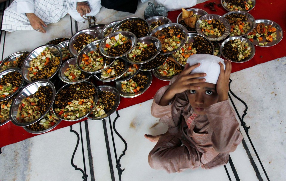 A boy adjusts his cap before preparing to eat his Iftar meal to break fast on the first day of Ramadan at a mosque in Delhi