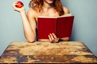 Naked woman reading and eating a peach