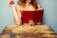 Naked woman reading and eating a peach