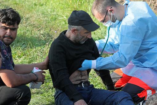 Ratownik pogotowia ratunkowego i członkowie grupy uchodźców odnalezionych na granicy polsko-białoruskiej w pobliżu miejscowości Usnarz Górny