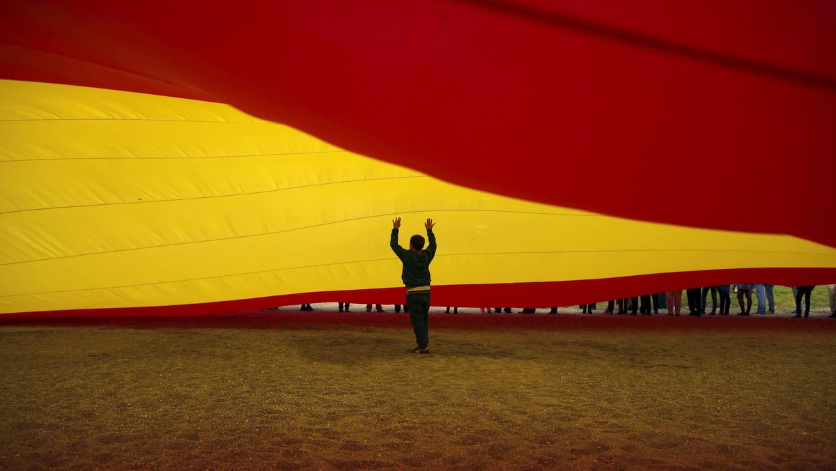 A child walks under a giant Spanish flag unfurled by supporters of Spain's Prime Minister Rajoy to s