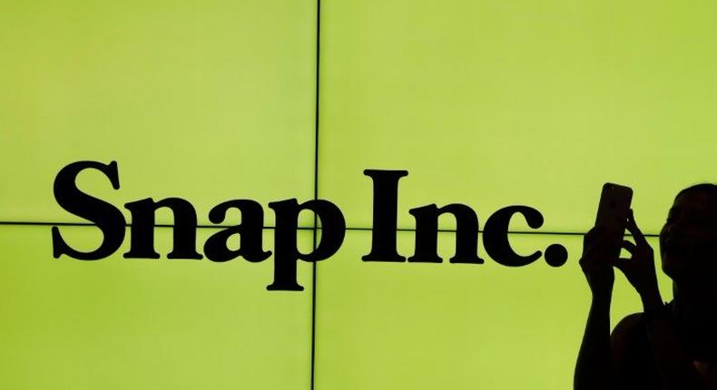 A woman stands in front of the logo of Snap Inc. on the floor of the New York Stock Exchange (NYSE) while waiting for Snap Inc. to post their IPO, in New York City