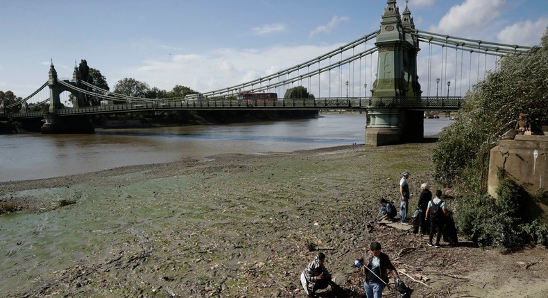 Volunteers work to clear rubbish from the banks of the River Thames, with Hammersmith Bridge in background.