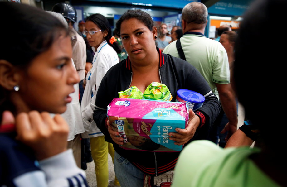 A woman holding food and other staple goods walks outside a supermarket in Caracas, Venezuela, June 30, 2016.