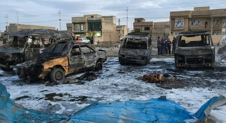 A picture taken with a mobile phone on February 16, 2017 shows burnt vehicles at the scene of a massive car bomb which killed dozens in a used car market in southern Baghdad