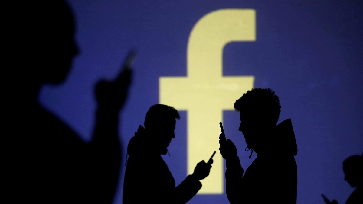 FILE PHOTO: Silhouettes of mobile users are seen next to a screen projection of Facebook logo in thi