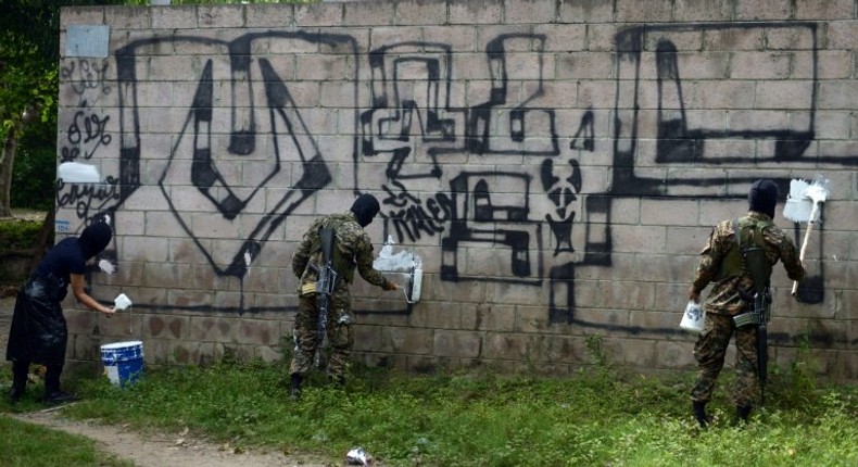 Police officers and soldiers paint over graffiti associated with the Mara Salvatrucha gang in Quezaltepeque, El Salvador