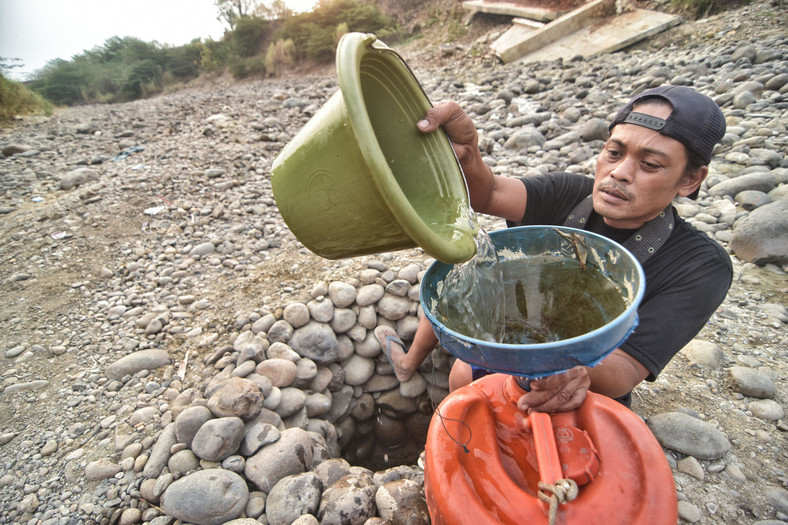 Mieszkaniec czerpie wodę z wyschniętej rzeki do użytku domowego, ponieważ jego studnie wysychają z powodu suszy w sezonie letnim. Eksperci ostrzegają, że El Nino pogorszy dotychczasowe problemy, Indonezja, 2019 r.