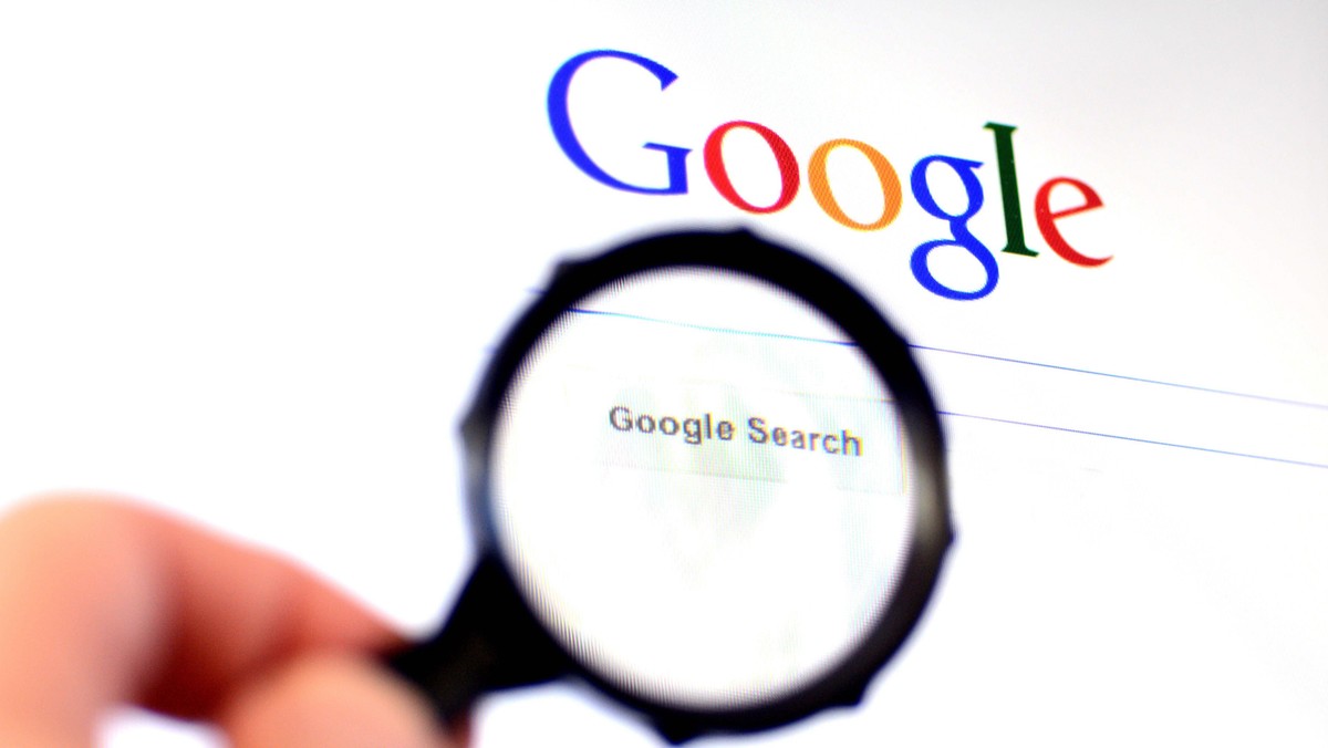 Hand holds Magnifying glass against Google homepage