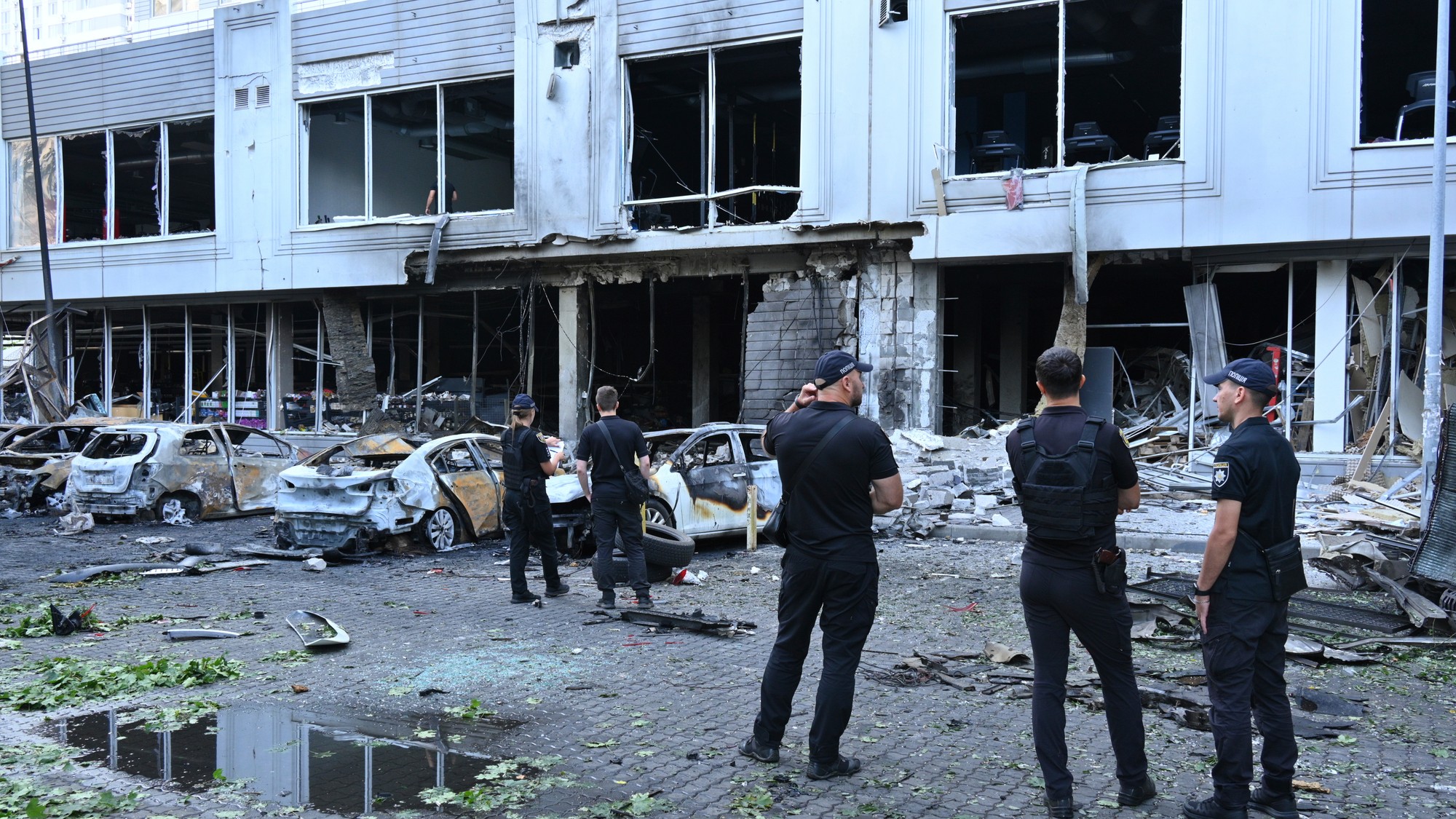 Policajti kontrolujú poškodené autá v obytnej štvrti po útoku ruského dronu v Odese.