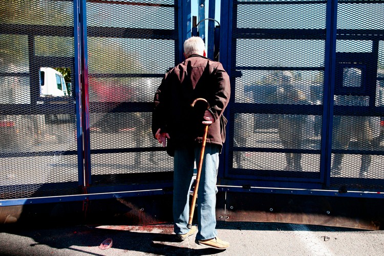 Starszy mężczyzna obserwuje zamieszki pod parlamentem w Atenach przez policyjną barykadę