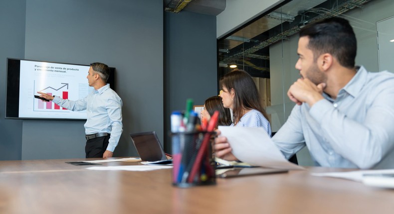 Man presenting graphs in PowerPoint slideshow to co-workers