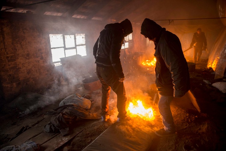 Uchodźcy z Afganistanu ogrzewają się przy ognisku rozpalonym w jednym z budynków w opuszczonym gospodarstwie rolniczym niedaleko granicy z Węgrami