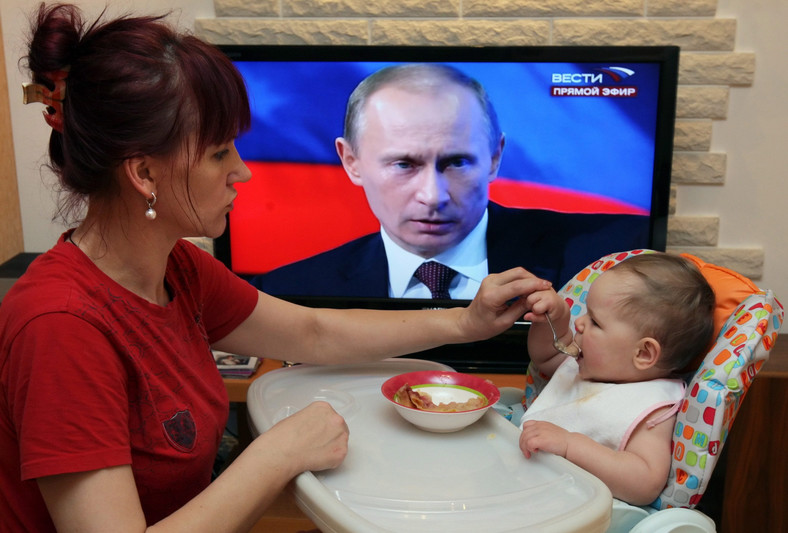 Kobieta karmi dziecko, w tle telewizor wyświetlający twarz Władimira Putina, Rosja, 3 grudnia 2009 r.