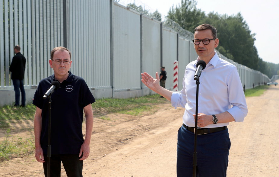 Minister Mariusz Kamiński i premier Mateusz Morawiecki przy ogrodzeniu na granicy Polski i Białorusi. Czerwiec 2022 r.