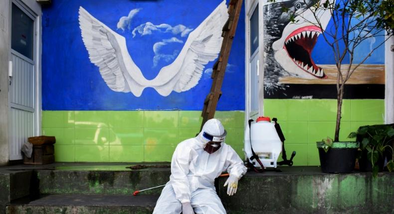 An Indonesian health agency official rests at the entrance to a public toilet as other colleagues conduct COVID-19 testing in Bandung, West Java