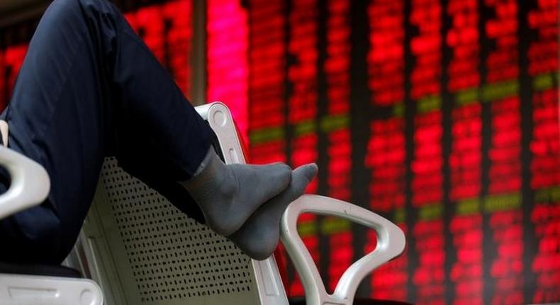 An investor puts his feet on a chair in front of an electronic board showing stock information at a brokerage house in Beijing, China, February 16, 2016.