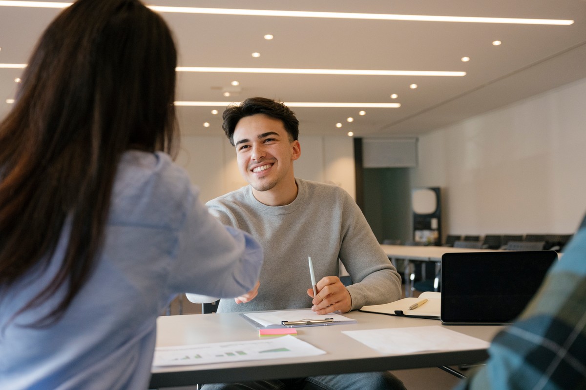 Young,Man,Smiling,While,Shaking,Hands,Across,A,Desk,With