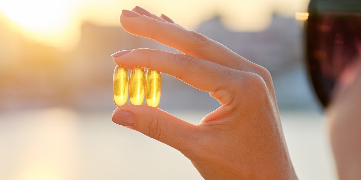 Yellow gel capsule vitamin d omega-3 in womans hand, sun sea background