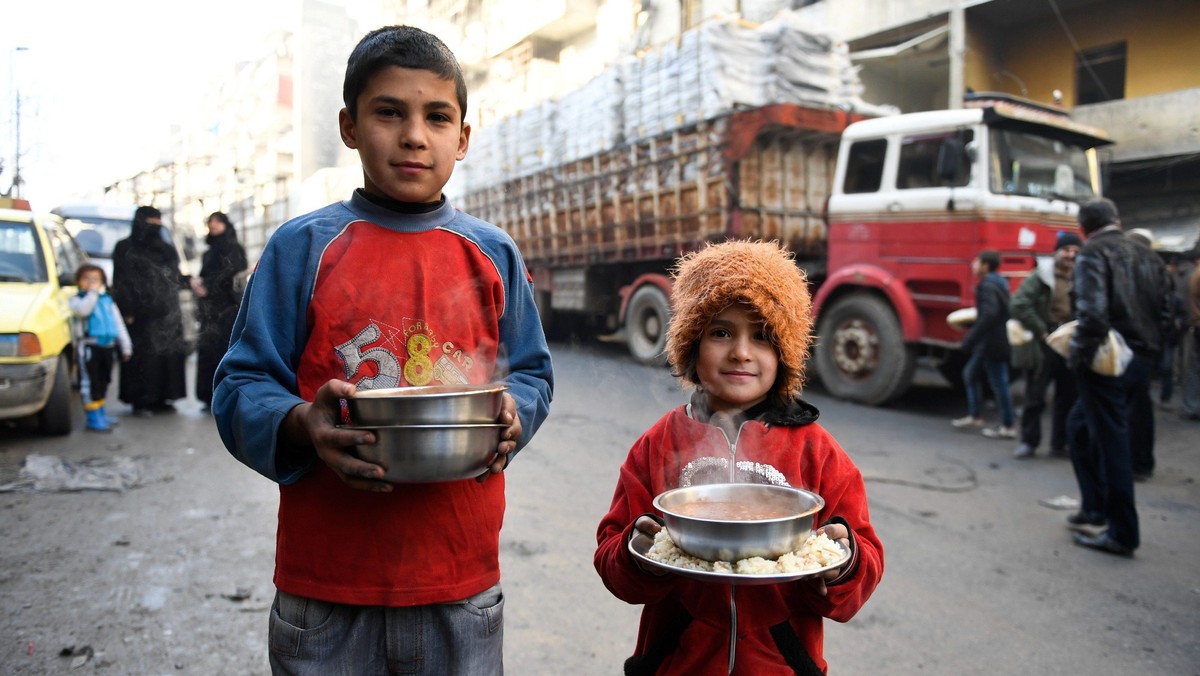 Children carry cooked meals provided by the UN through a partner NGO at al-Mashatiyeh neighborhood o