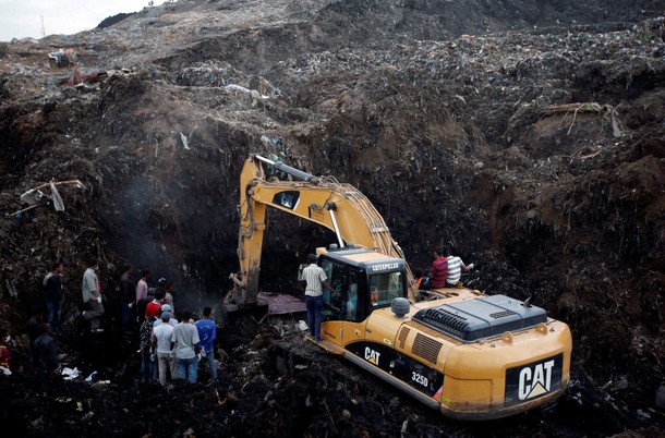 Rescue workers watch as excavators dig into a pile of garbage in search of missing people following 