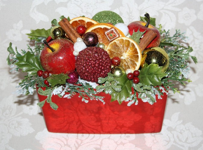 Stroik na stół w typowo świątecznych tonacjach: czerwieni i zieleni, wzbogacony suszonymi owocami, laskami cynamonu i ozdobnymi jabłuszkami. Autorka: Marta Jarosińska-Mańka