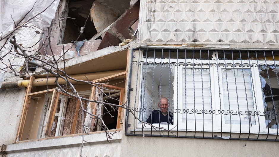 Mężczyzna sprzątający swoje mieszkanie w bloku mieszkalnym, który został uszkodzony i częściowo spalony po ataku rakietowym. Charków, Ukraina 2022 r.