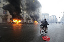 A man rides a bicycle in front of burning cars during a rally against Expo 2015 in Milan