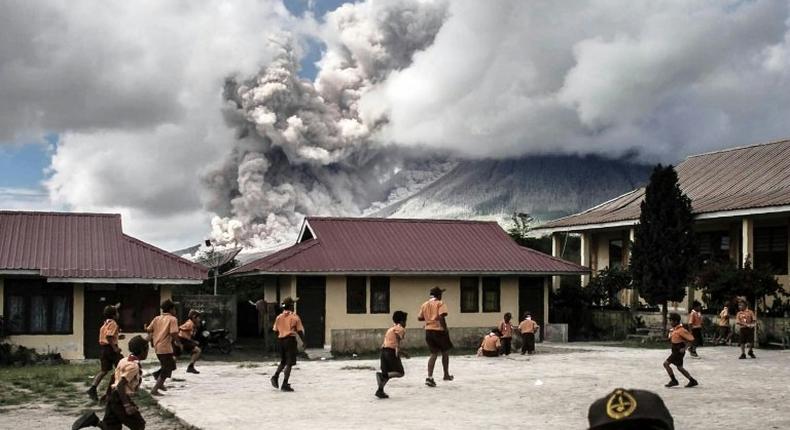 Children play at school as Indonesia's Mount Sinabung spews clouds of smoke and ash on February 10, 2017