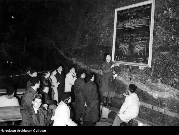 Przewodnik stojący przy tablicy informacyjnej zapoznaje zwiedzających z mechanizmem funkcjonowania kopalni, rok 1939