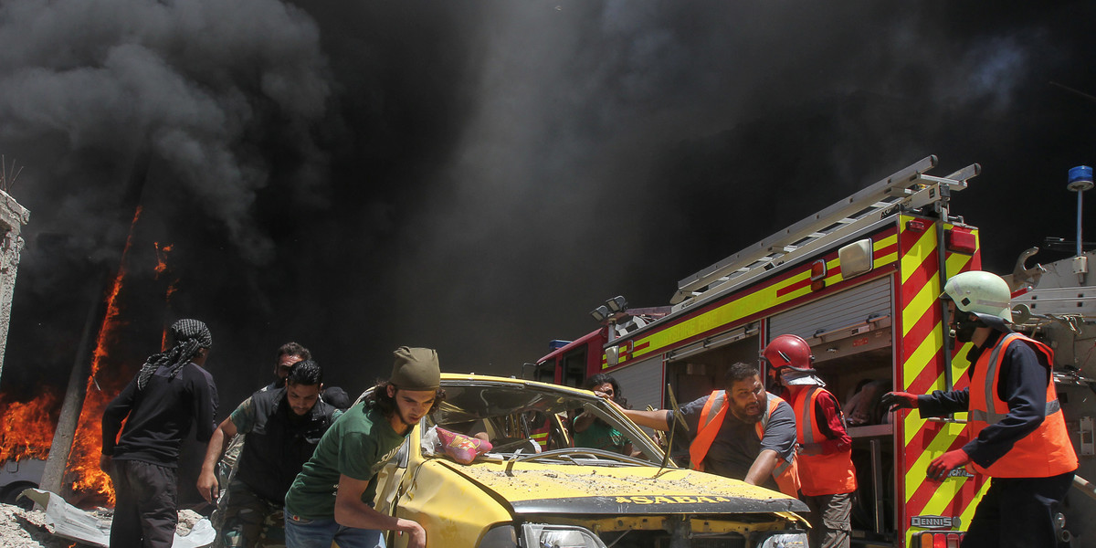 Civil defense members and rescuers push a car at a site hit by air strikes in Idlib, Syria.