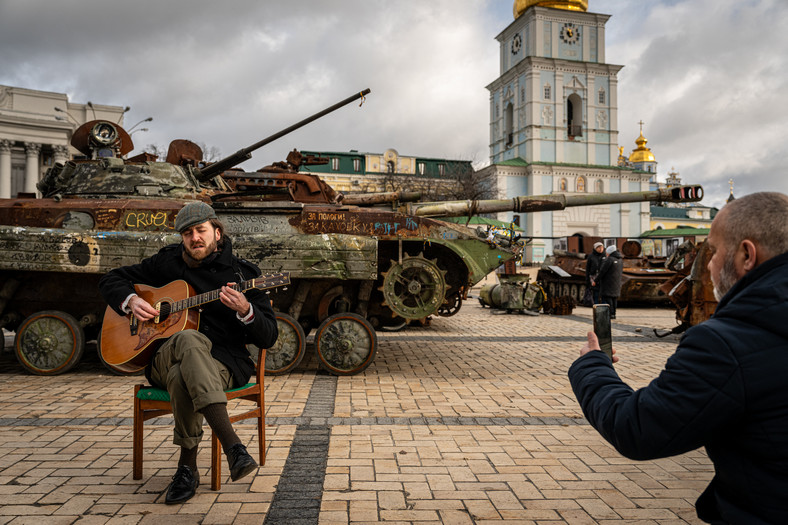 Mężczyzna gra na gitarze obok zniszczonych rosyjskich czołgów wystawionych na placu przed Klasztorem Św. Michała o Złotych Kopułach w Kijowie, luty 2023 r.